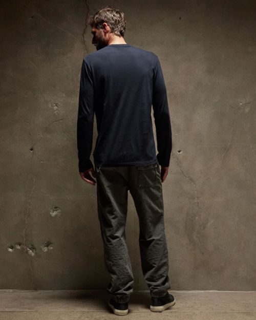 The back view of man in a long sleeve crew neck cotton shirt posing against a wall.