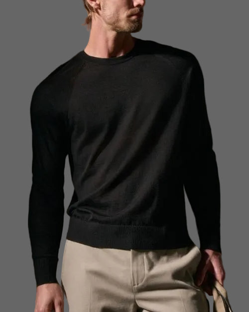 A man wearing a black cashmere sweater and khaki pants stands confidently.