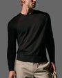 A man wearing a black cashmere sweater and khaki pants stands confidently.