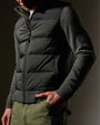 A man wearing a two-tone olive and black zip-up sweater with olive pants stands confidently.
