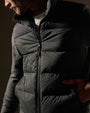 A man dressed in a black and olive zip-up sweater poses casually.
