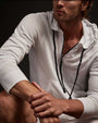 A man in a white hoodie sits against a black background, showcasing a lightweight vintage French Terry zip-up design.