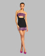 Black mini dress with cut-out detail around the waist and a purple sequined pattern on both the bust area and the lower half of the garment. Styled with purple high-heeled shoes.