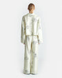 The backside view of a person wearing a matching pajama set consisting of a long-sleeve button-up shirt and pants. The pajama set is off-white with black line drawings of various A person is seen wearing a matching pajama set consisting of a long-sleeve button-up shirt and pants. The pajama set is off-white with black line drawings of various whimsical characters and scenes such as warriors on horses and towers. The background is plain white.