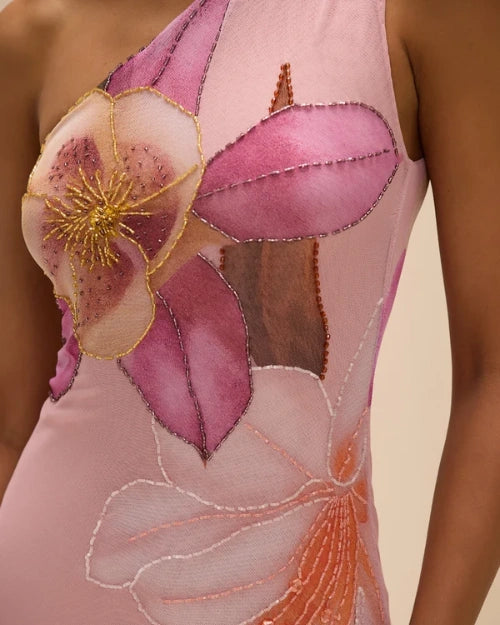 Close-up detail of a blush pink one-shoulder midi dress featuring oversized floral embroidery and beaded embellishments in pink, peach, and gold tones.