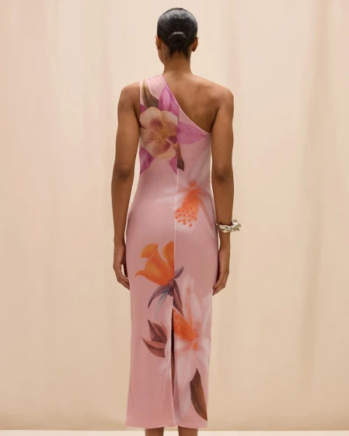 Back view of a pink one-shoulder midi dress featuring oversized floral prints in pink, orange, and white tones, shown on a model against a neutral studio background.