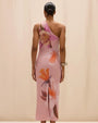 Back view of a pink one-shoulder midi dress featuring oversized floral prints in pink, orange, and white tones, shown on a model against a neutral studio background.