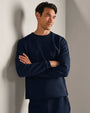 Person wearing a navy long-sleeve performance crewneck shirt with textured fabric, styled with matching athletic pants in a modern indoor setting.