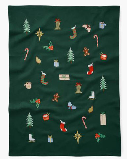 Festive tea towel with Christmas motifs on a green background, featuring gingerbread men, stockings, candy canes, trees, gifts, and stars, creating a joyful holiday feel.