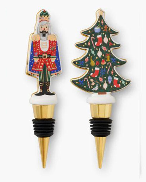 Two festive bottle stoppers shown: one shaped like a nutcracker in colorful attire and another like a Christmas tree adorned with ornaments. Bright and cheerful.