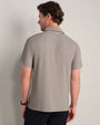 Back view of a light taupe short-sleeve polo shirt featuring a classic collar, textured fabric and relaxed modern fit.