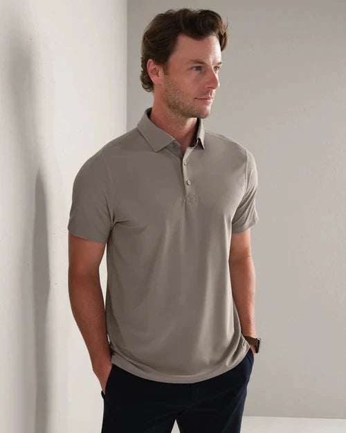 Person wearing a light taupe short-sleeve polo shirt with a three-button placket, styled with dark trousers in a modern lifestyle setting.