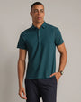 Men's teal performance polo shirt with short sleeves, classic collar, and modern fit, paired with navy pants on a neutral studio background.
