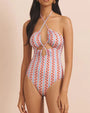 Model wearing a one piece swimsuit with cut-outs in the chest area, with strings crossing at the chest and tying at the back of the neck. The one-piece features a orange, blue and pink pattern. 