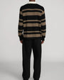 Back view of a long-sleeve rugby-style knit polo sweater with black and brown horizontal stripes and a contrasting cream collar, paired with black wide-leg trousers.