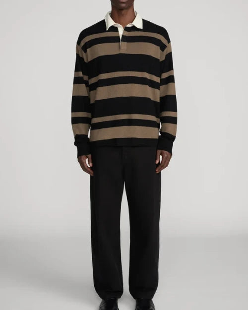 Model wearing a black and brown striped long-sleeve rugby polo sweater with a contrasting cream collar, paired with relaxed black trousers against a light gray background.