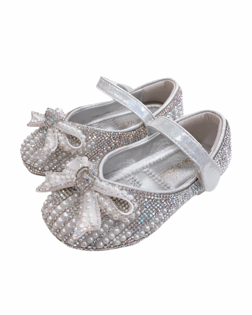 A pair of little girls silver shoes covered in rhinestones and pearls featuring a decorative bow on the toe, elegantly designed for formal occasions.