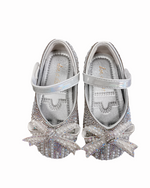 A pair of silver little girls shoes covered in rhinestones and pearls featuring a decorative bow on the toe, elegantly designed for formal occasions.