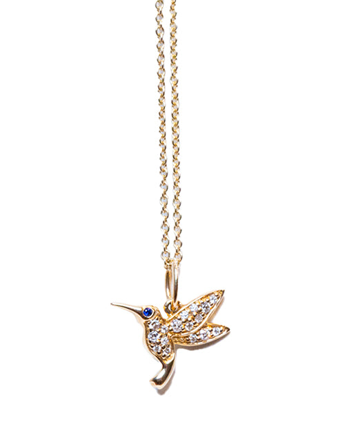 Small Humming Bird charm necklace in yellow gold & pave diamonds and eye id blue sapphire on a white background.