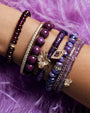 Model arm showing multiple shades of purple precious stones and Amethyst heishi stone bracelet with magnolia charm in pave diamonds and yellow gold.