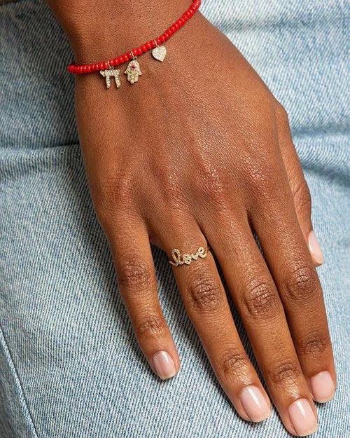 Hand model showing Love script ring in yellow gold and pave diamonds, and a beaded bracelet with 3 sydney evan charms.