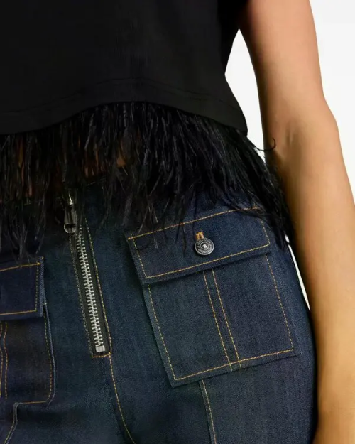 Close-up of dark denim pants with patch pockets and a black fringed top.