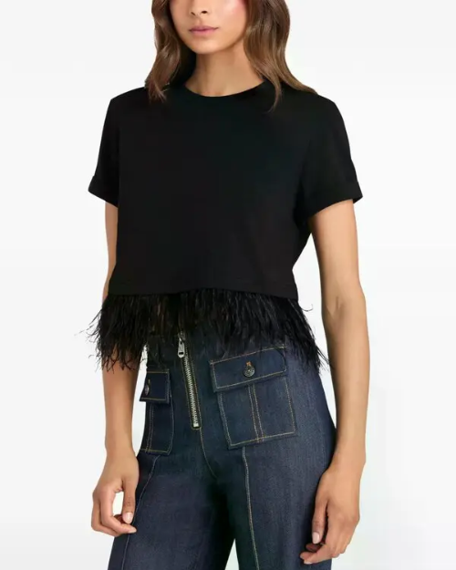 Person wearing a black top with feather trim and dark denim pants.