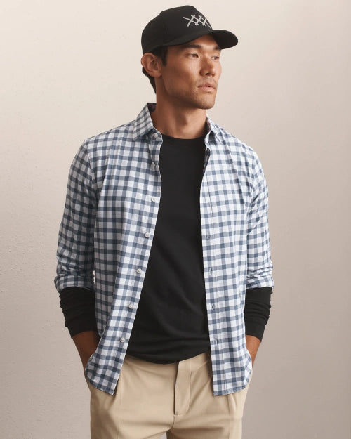 Person wearing a blue and white gingham check button-down shirt layered over a black crew neck shirt with khaki trousers.