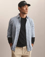 Person wearing a blue and white gingham check button-down shirt layered over a black crew neck shirt with khaki trousers.