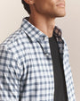 Close-up of a men's blue and white gingham check button-down shirt featuring a classic collar, button-front closure, and lightweight woven fabric.