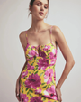 Woman with a yellow, thin strapped dress with pink flowers against a grey background.