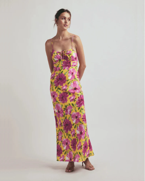 Woman with a yellow dress with pink flowers against a grey background.