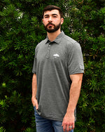 Man wearing Heating Up Golf Polo in grey in front of bush/tree background.