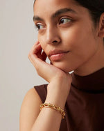 The  woman has her right hand under her chin with a gold chain bracelet on her wrist.