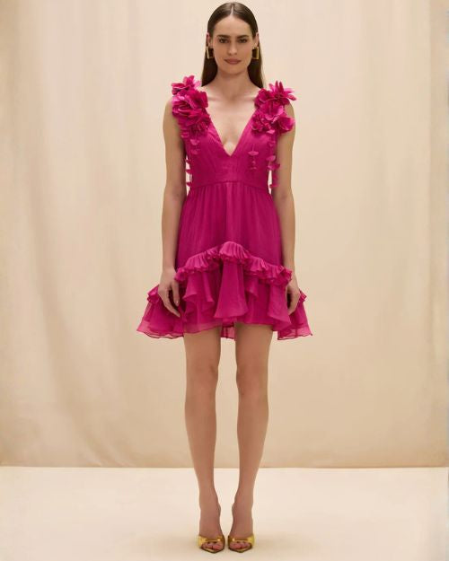 A woman in a pink Patbo Chiffon Carmen Flowers mini dress featuring a ruffled hem, showcasing a stylish and feminine look.