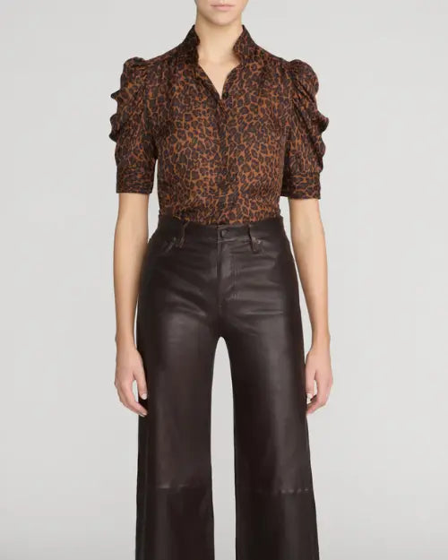 Model wearing a brown and black leopard-print blouse with a high open collar, ruffle-trimmed puff sleeves, and elbow-length fitted cuffs, paired with high-waisted dark brown leather wide-leg pants against a light gray background.


