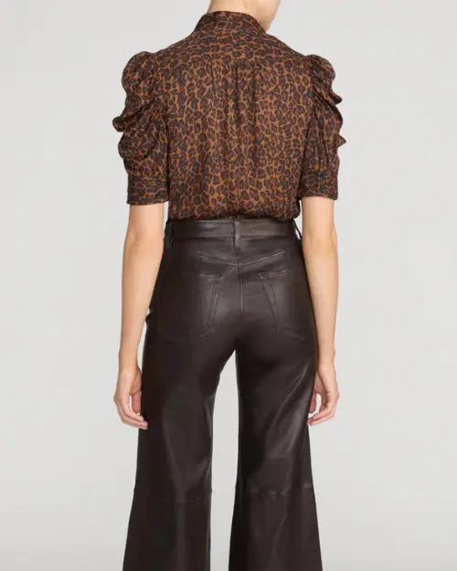 Back view of a brown and black leopard-print blouse featuring a high collar, gathered shoulders, and ruffle-trimmed elbow-length sleeves, tucked into high-waisted dark brown leather wide-leg pants, shown against a light gray background.


