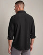 Back view of a charcoal long-sleeve button-down shirt with a classic collar and tailored fit, paired with light gray pants against a neutral background.