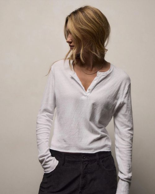 A woman wearing a long sleeve white cotton shirt and black pants stands confidently.