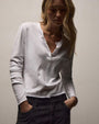 A woman dressed in a white cotton long-sleeve shirt and black pants poses elegantly.