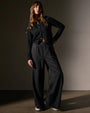The model is dressed in lightweight black linen pants paired with a black top, presenting a sleek and modern look.