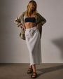 The model displays a trendy cropped top and a flowing high-low white linen skirt, perfect for warm weather.