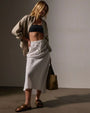 A woman in a white high-low linen skirt and crop top poses elegantly, embodying a fresh and fashionable.