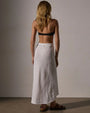 Back view of a woman wearing a high-low white linen skirt, showcasing its flowing design and lightweight fabric.