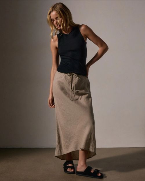 A model showcases a black top paired with a high-low linen skirt.