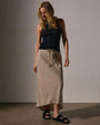 A model in a black tank top paired with a high-low linen skirt.