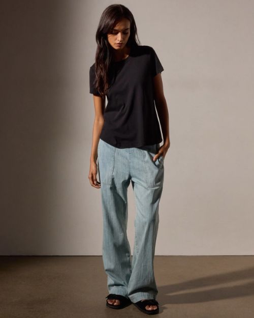 A model showcases a ladies' black crop tee shirt paired with blue denim pants.
