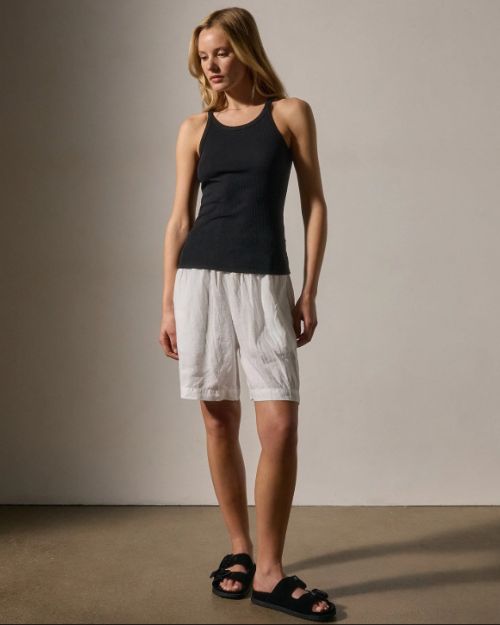 A woman wearing a black cotton tank top and white shorts stands confidently.