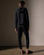 Back view of a woman in black sweatpants and a cashmere black track jacket, standing casually.