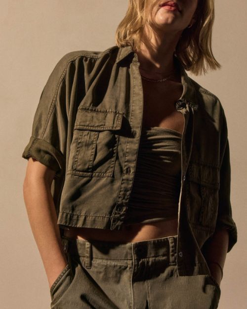 A woman wearing a stylish birch-colored cropped shirt. and pants stands confidently.